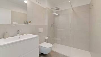 A modern bathroom with a white sink, toilet, and shower area.