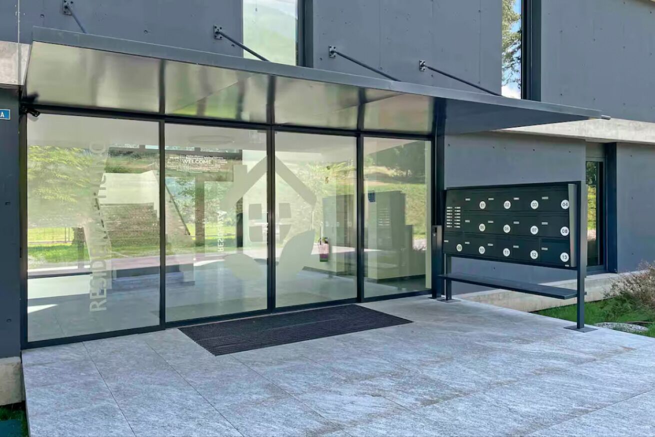 A modern building entrance with glass doors, a metal gate with numbered slots, and a clear view of the surrounding area.