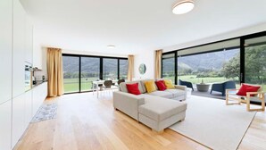 A spacious living area with a large sofa, dining table, and chairs. There are large windows offering a view of the outdoors. - An oasis of peace in nature (Hydra 06 Residenza Ticino) (Bellinzona)