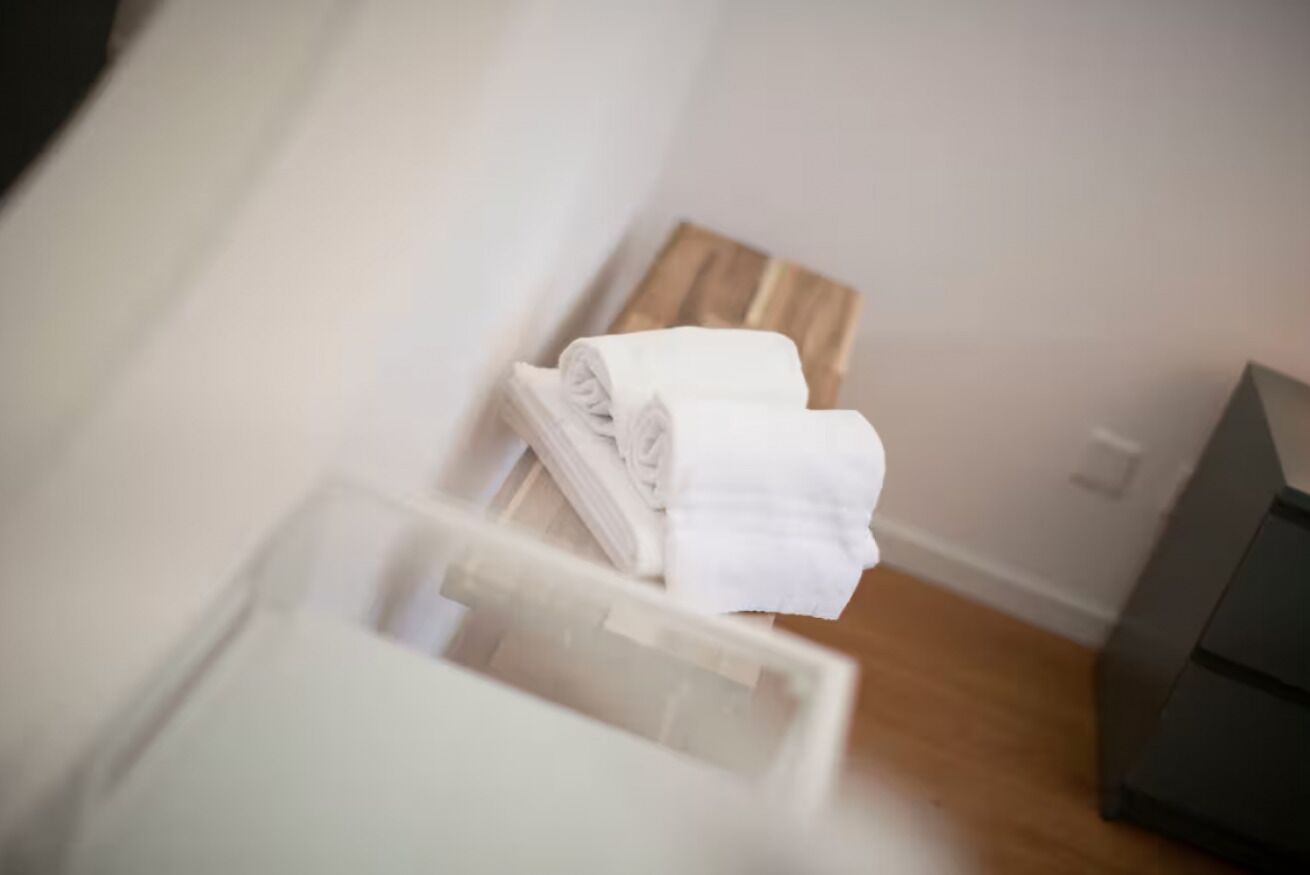 Ein aufgeräumtes Badezimmer mit einer hölzernen Sitzbank, einem weißen Handtuch und einem sichtbaren Duschbereich.