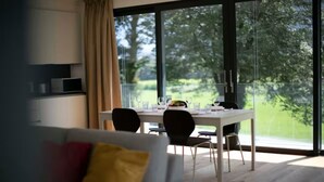 A modern dining area with a table set for four, large windows, and a view of a green landscape. - An oasis of peace in nature (Hydra 06 Residenza Ticino) (Bellinzona)