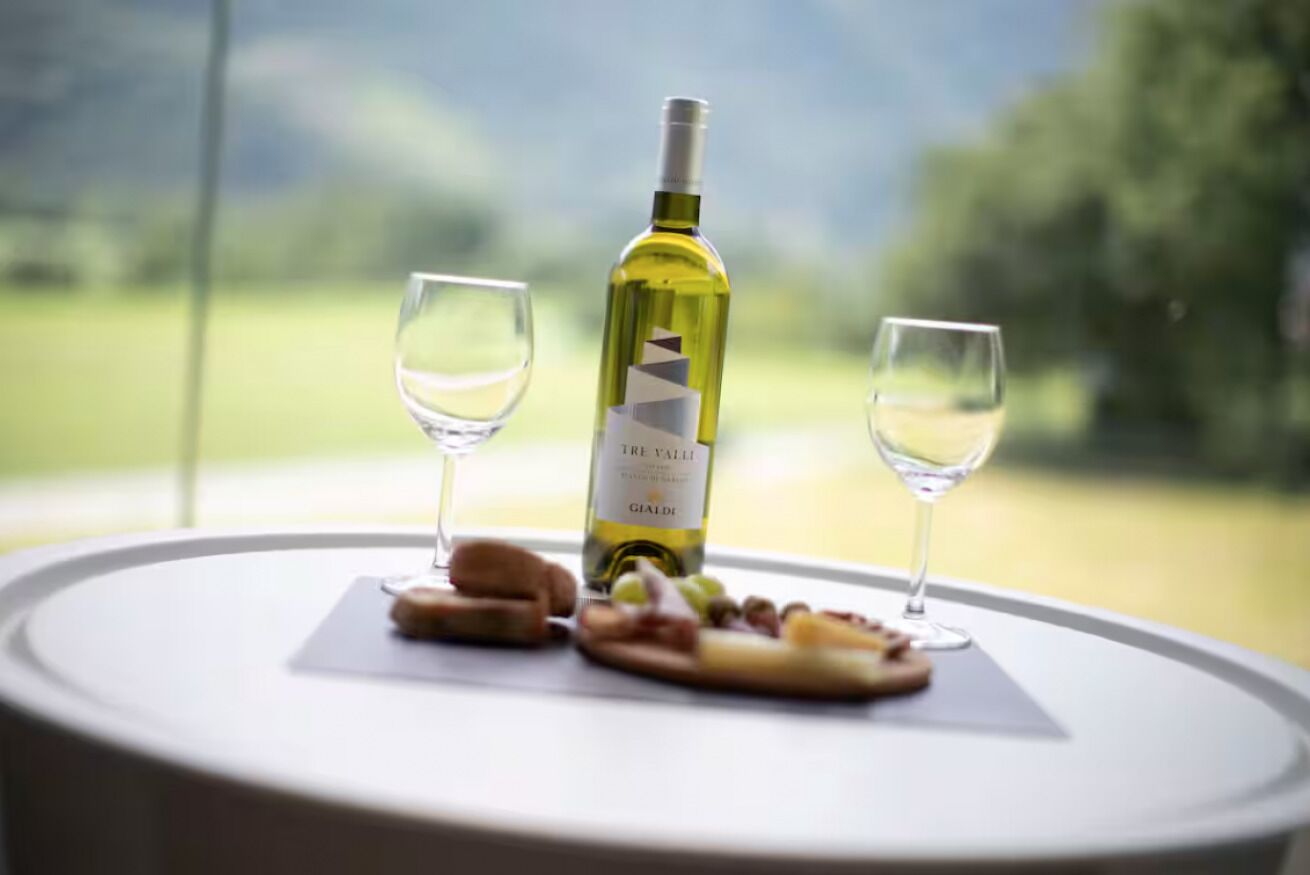 Eine Flasche Tre Valli Gialde Wein auf einem Tisch mit zwei Gläsern und einem Teller mit Essen.
