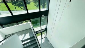 A modern staircase with glass railings and a view of a green outdoor area. - An oasis of peace in nature (Hydra 06 Residenza Ticino) (Bellinzona)