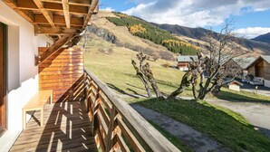 Ein Holzbalkon mit Blick auf eine gebirgige Landschaft und ein kleines Gebäude in der Ferne.