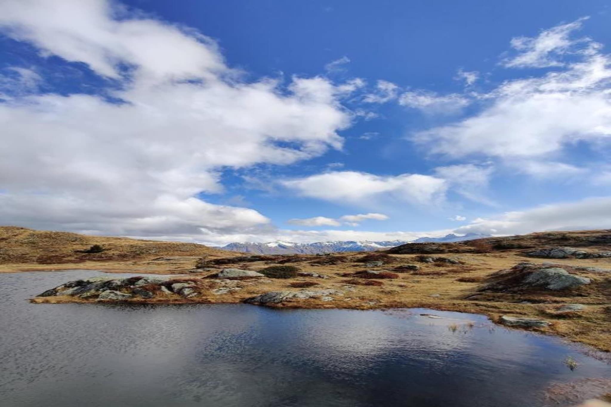 A natural landscape with a lake, rocky terrain, and distant mountains under a partly cloudy sky.