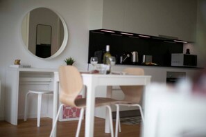 A modern kitchen with white cabinetry, a round mirror, and a dining area with a white table and chairs. - An oasis of peace in nature (Lyra 08 Residenza Ticino) (Bellinzona)