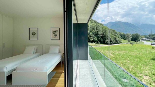 Ein modernes Schlafzimmer mit zwei Betten, einem Balkon mit Glasgeländer und Blick auf die Berge.