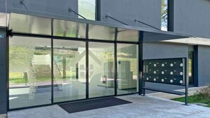 Ein moderner Gebäudeeingang mit großen Glasüren, einem Metallgitter mit nummerierten Schließfächern und einer gepflasterten Fläche davor.