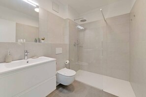 A modern bathroom with a large mirror, a white sink, a toilet, and a glass-enclosed shower area. - An oasis of peace in nature (Lyra 08 Residenza Ticino) (Bellinzona)