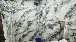 Une salle de bain avec un mur en marbre, une douche, un lavabo et des toilettes.