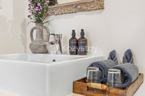 A bathroom with a bathtub, a vase with flowers, two bottles of lotion, and a wooden tray with glasses and towels. - Amaya Villa by Kozystay - Canggu (Canggu)