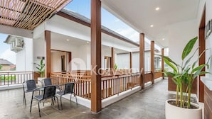 A covered outdoor area with a seating arrangement, wooden columns, and potted plants. - Amaya Villa by Kozystay - Canggu (Canggu)