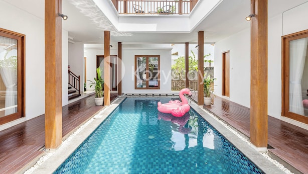 A swimming pool with a pink flamingo float, wooden pillars, and a balcony with chairs. - Amaya Villa by Kozystay - Canggu (Canggu)
