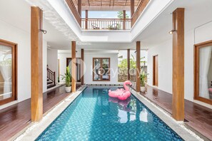 A swimming pool with a pink flamingo float, wooden pillars, and a balcony with chairs. - Amaya Villa by Kozystay - Canggu (Canggu)