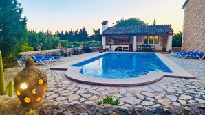 Une piscine avec une terrasse en pierre, un petit bâtiment doté d’un toit en tuiles et une décoration à base de cactus.