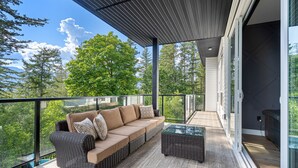 A balcony with a sofa and a coffee table, overlooking a forested area.
