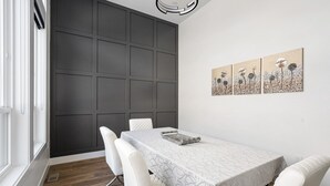 A modern dining room with a dark paneled wall, a white table with a patterned tablecloth, and three framed artworks on the wall.