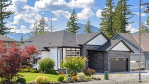A residential house with a stone facade, a garage, and a well-maintained front yard with various plants and trees.