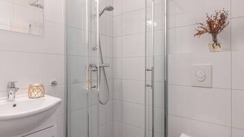 A modern bathroom with a glass-enclosed shower, a white sink, and a toilet.