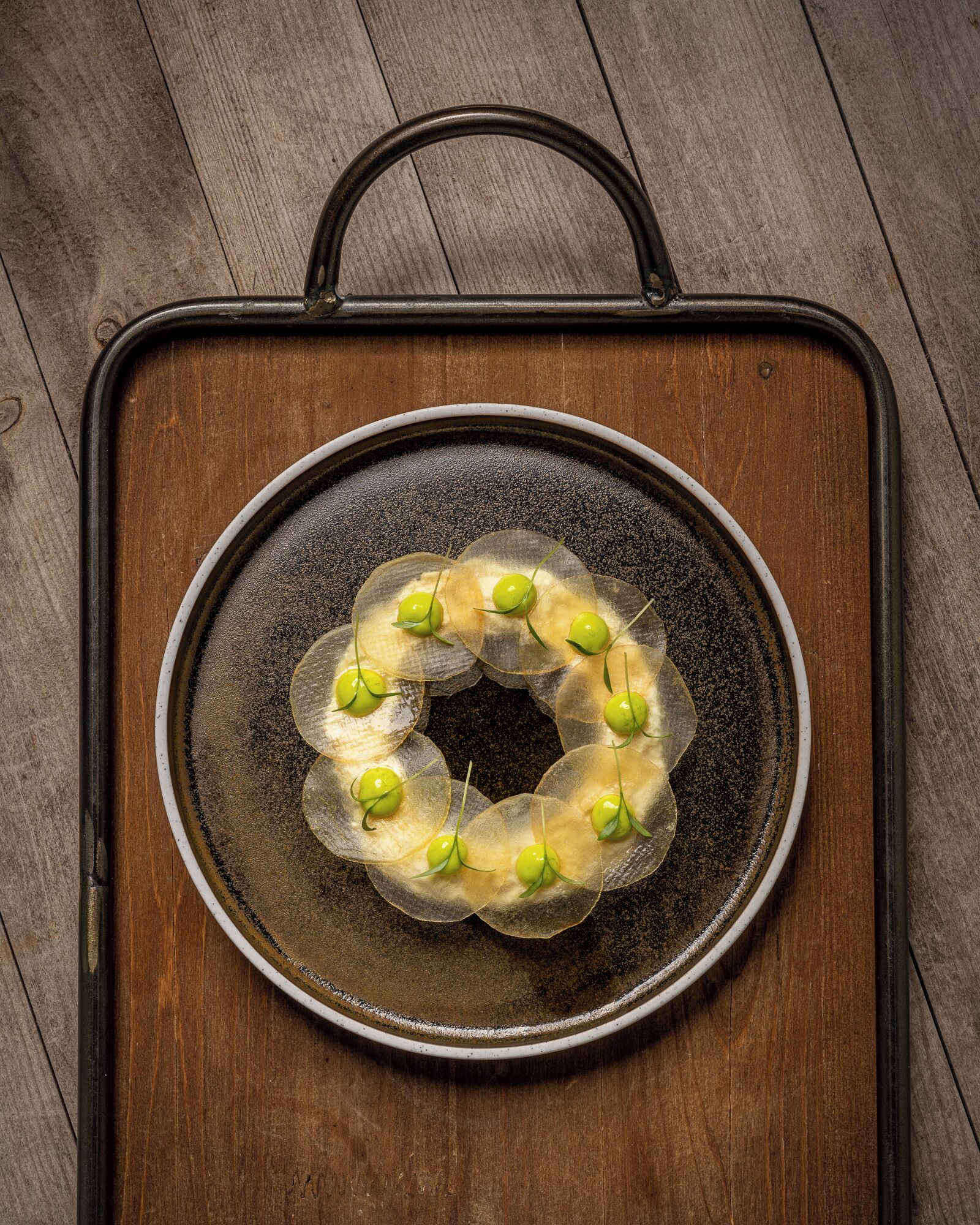 A round, black tray with a handle on top, placed on a wooden surface.