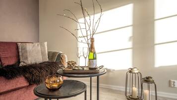 A cozy living room with a sofa, a small round table, a bottle of champagne, and two candle lanterns.