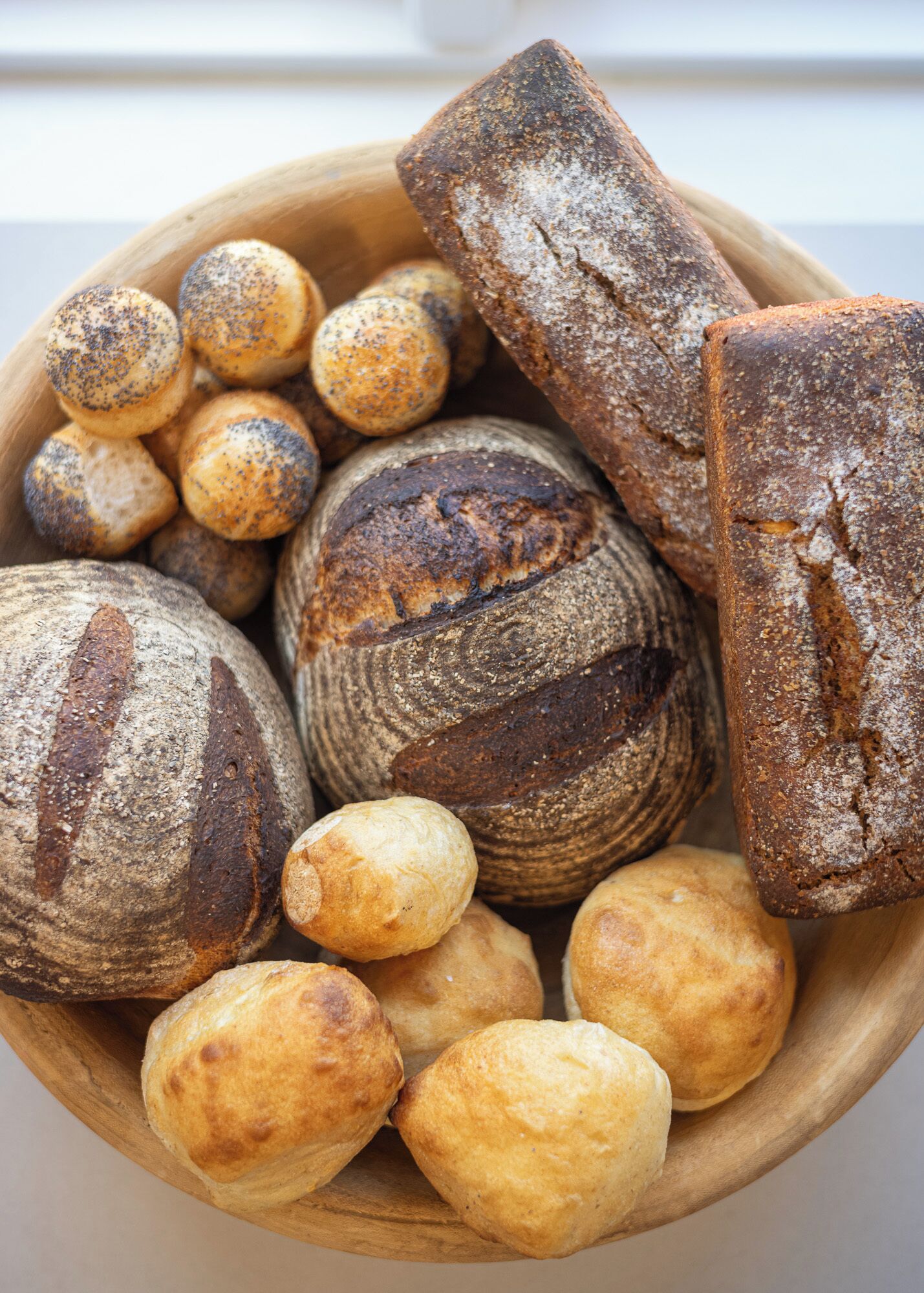 Una ciotola di legno piena di diversi tipi di pane, tra cui pagnotte rotonde e baguette.
