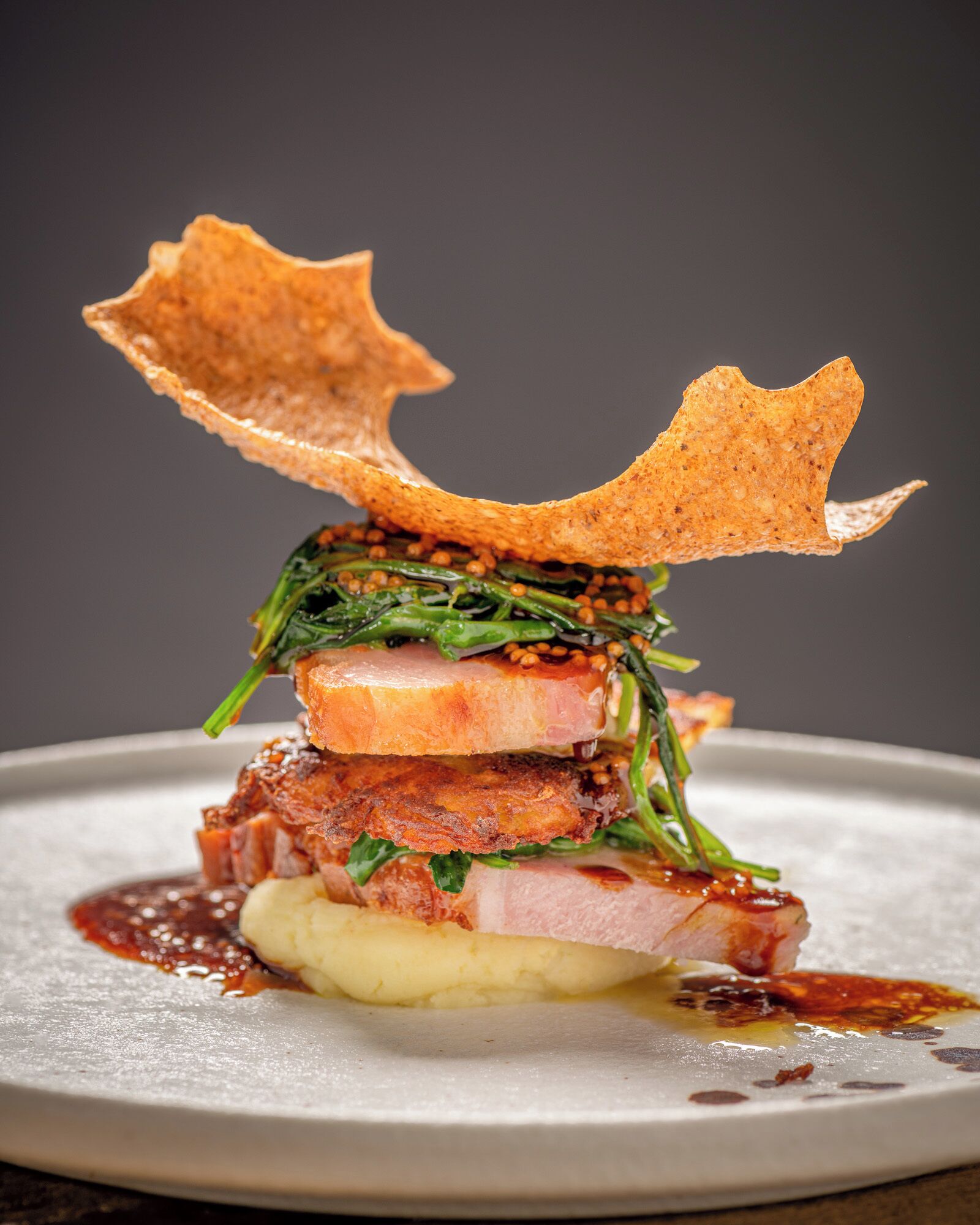 A dish with various food items including meat, greens, and a crispy element on a plate.