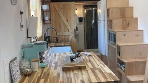 A modern kitchen with a wooden island, black chairs, and a staircase leading to a loft. - Mountain Top Tiny House by Beyond Expectations: 1BR w/ Mountain Views (Sevierville)