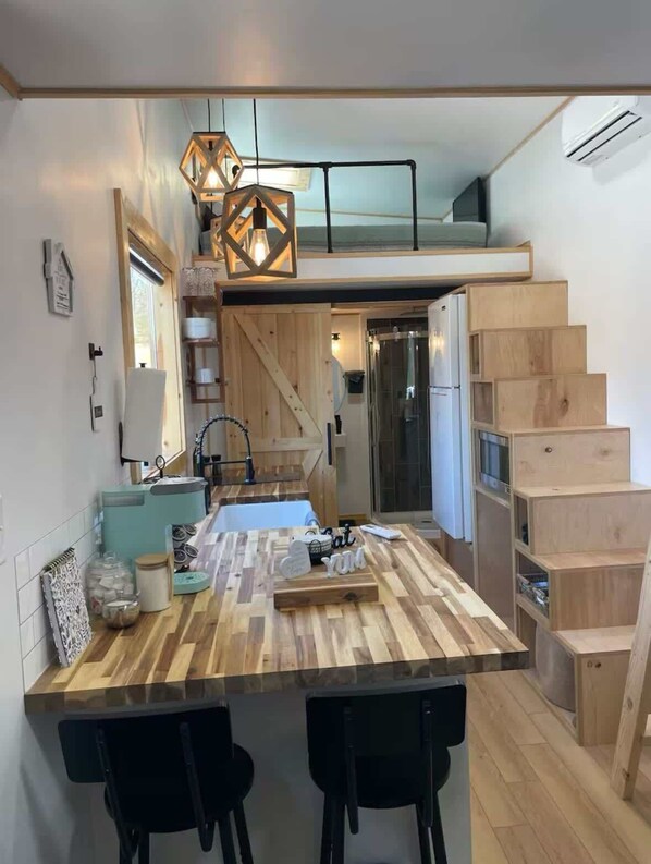 A modern kitchen with a wooden island, black chairs, and a staircase leading to a loft.