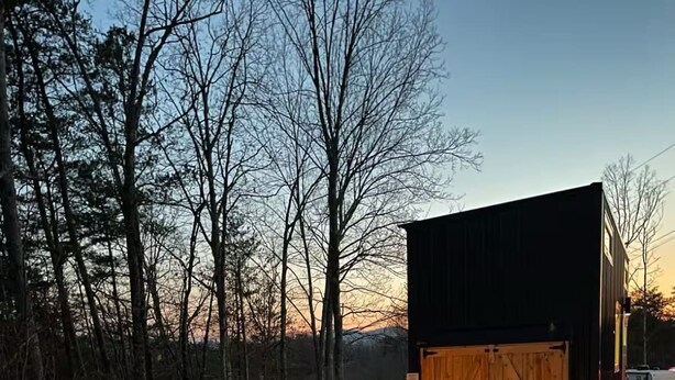 A cozy outdoor seating area with Adirondack chairs and a fire pit, surrounded by gravel and trees. - Mountain Top Tiny House by Beyond Expectations: 1BR w/ Mountain Views (Sevierville)