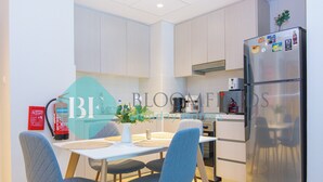Une cuisine moderne avec un coin repas, comprenant un réfrigérateur en acier inoxydable, des meubles blancs et des chaises bleues.