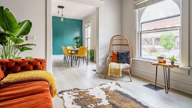 Ein modernes Wohnzimmer mit Essbereich, einem großen Fenster und einem einzigartigen grünen Akzent an der Wand.