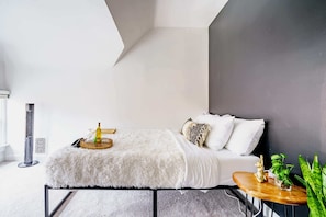 A modern bedroom with a bed, bedside table, and a small plant.