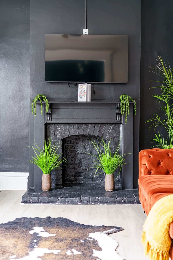 A modern living room with a fireplace, a flat-screen TV mounted above it, and two potted plants on either side.
