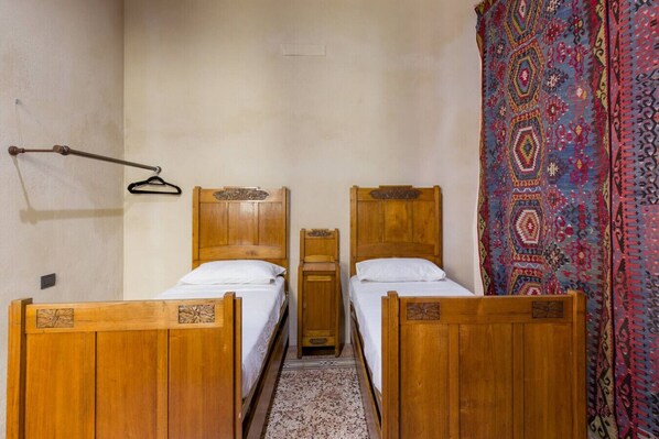 A room with two wooden beds, a small wooden cabinet, and a colorful patterned curtain.