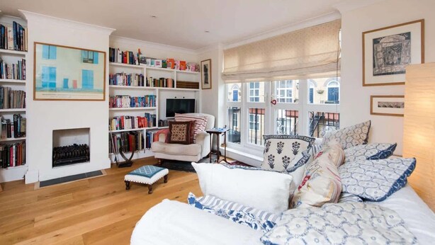 Een ruime woonkamer met een open haard, een grote boekenkast, een comfortabele bank en uitzicht op het omliggende landschap door grote ramen.