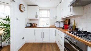 Een moderne keuken met witte kasten, een houten aanrecht, een gasfornuis en een raam met zonwering.
