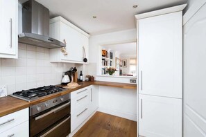 A modern kitchen with white cabinetry, a gas stove, an oven, and a stainless steel range hood. - Lovely Central London 2 Bedroom Family Home (London)