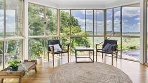Ein geräumiges Zimmer mit großen Fenstern, zwei Stühlen, einem kleinen Tisch und einem gewebten Teppich.