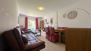 A living room with a brown leather sofa, a wooden dining table with red chairs, a TV, and a clock on the wall. - Apartment Josefa Summ (Vale de Parra)