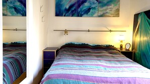Une chambre à coucher avec un lit, une table de chevet, une lampe et un miroir. Les murs sont ornés de tableaux abstraits.