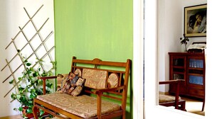 Une pièce avec un banc en bois adossé à un mur vert, un plancher en bois et une porte donnant sur une autre pièce.