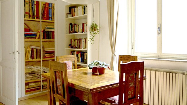 Une pièce avec une table en bois, quatre chaises, une bibliothèque et une plante suspendue.