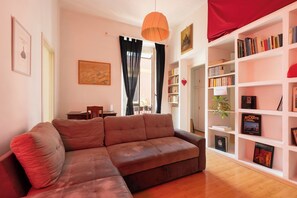 A living room with a brown sofa, a bookshelf filled with books, and a painting on the wall.