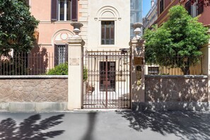 A gated entrance with a stone wall, a metal gate, and a building with a classical architectural style. - Vacation Home Two Steps from the Vatican - Comfort and Metro Ottaviano Under House (Roma)