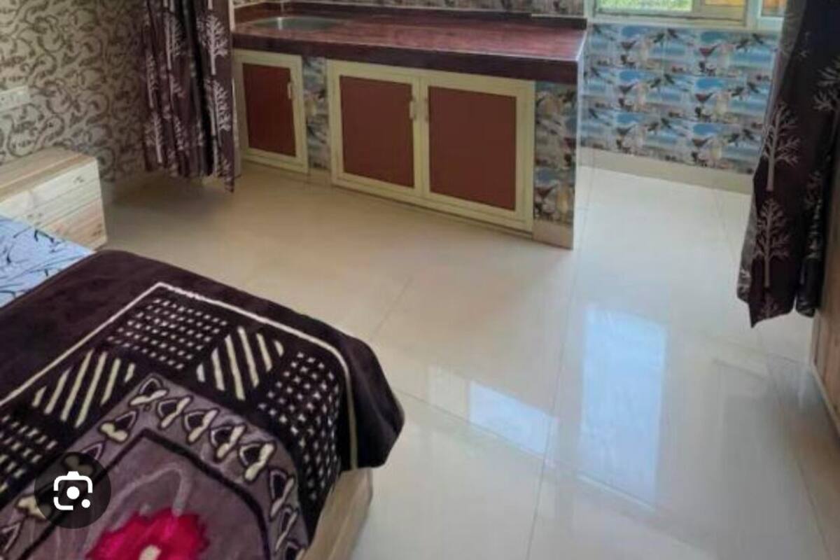 A bedroom with a large arched window, a bed, and a small kitchenette area.