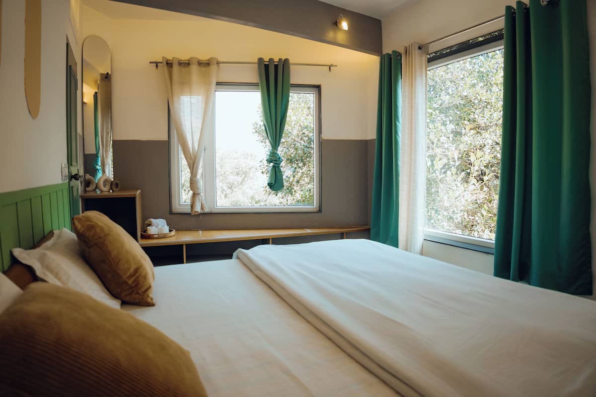 A bedroom with a bed, a bedside table, a mirror, and a window with curtains.