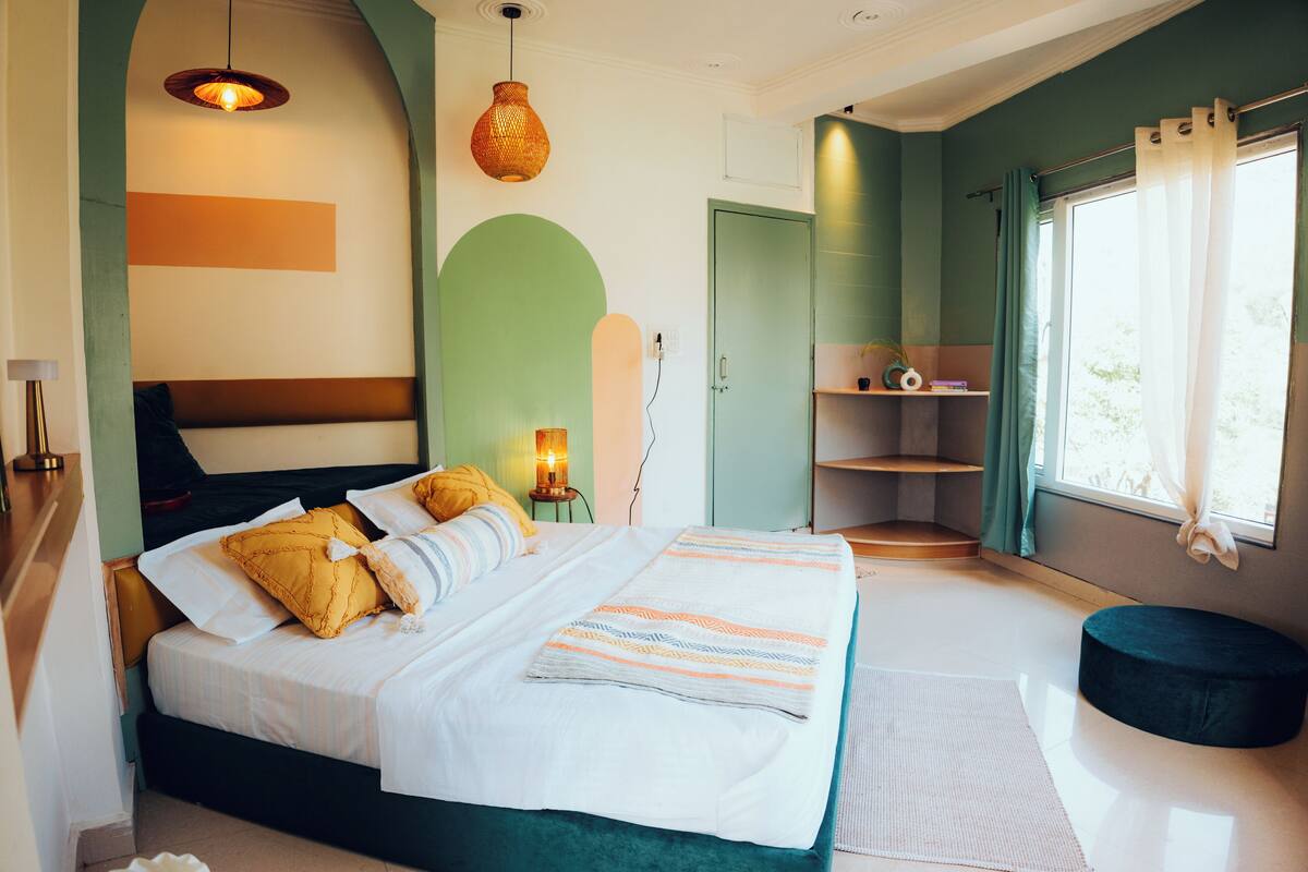 A modern bedroom with a bed, bedside lamp, and a view of the outdoors.