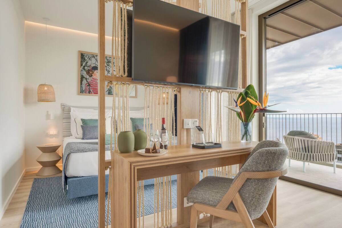 Ein modernes Hotelzimmer mit Balkon, Flachbildfernseher, Schreibtisch aus Holz und einer gemütlichen Sitzecke.