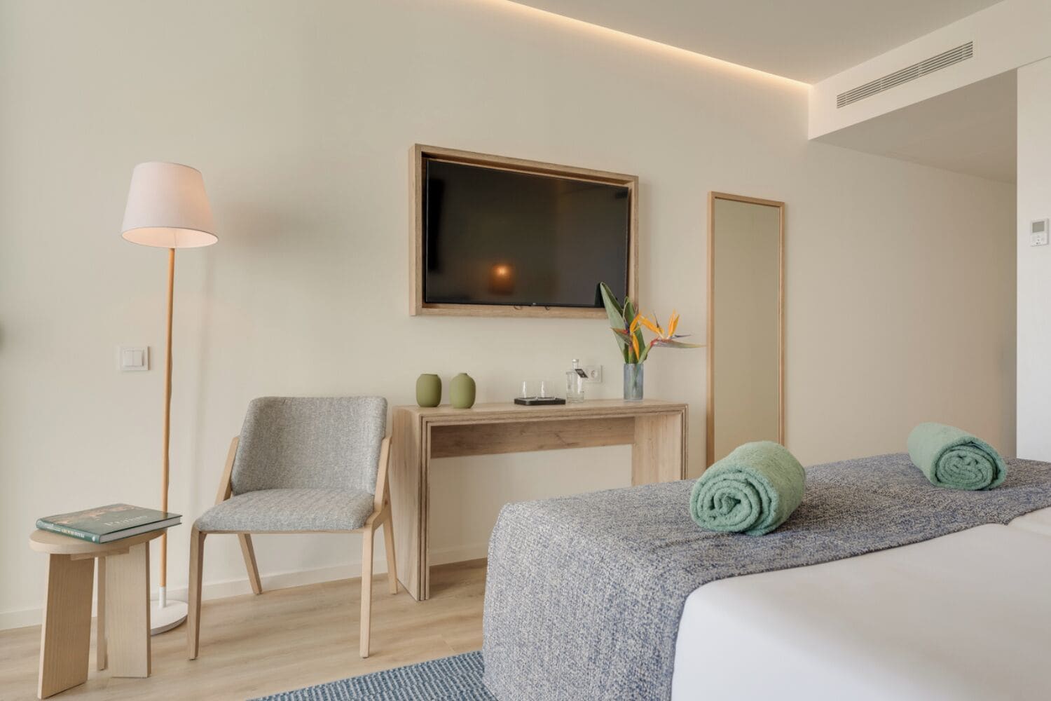 A hotel room with a bed, a desk, a chair, a TV, and a mirror.